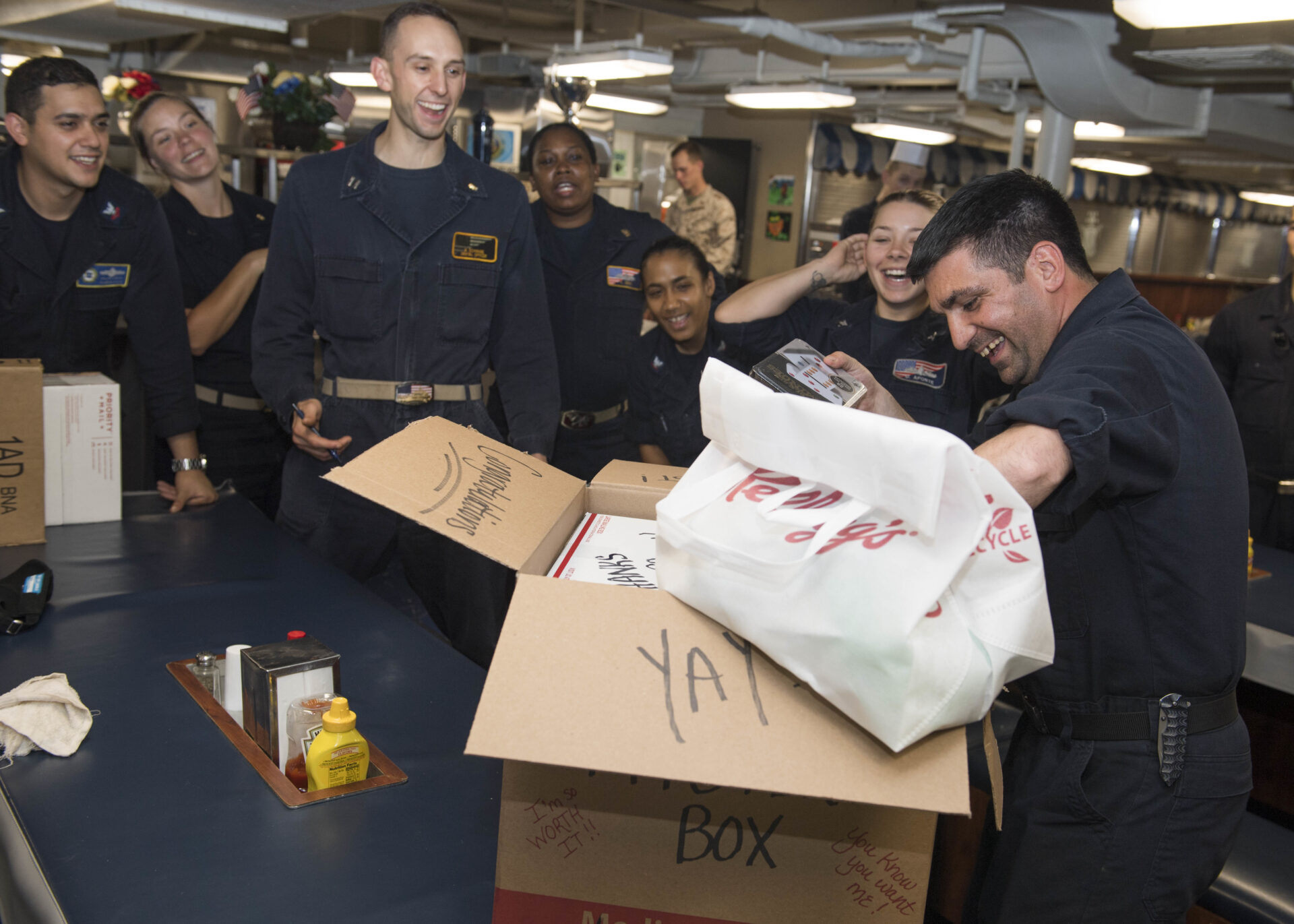 180505-N-TJ319-0127
U.S. 5TH FLEET AREA OF OPERATIONS (May 5, 2018) Boatswain's Mate 2nd Class Jonathan Giguere, right, opens a mystery care package as part of a family readiness group sponsored raffle aboard the Harpers Ferry-class dock landing ship USS Oak Hill (LSD 51). Oak Hill is homeported in Virginia Beach, Va., and is deployed the U.S. 5th Fleet area of operations in support of maritime security operations to reassure allies and partners, and preserve the freedom of navigation and the free flow of commerce in the region. (U.S. Navy photo by Mass Communication Specialist 3rd Class Jessica L. Dowell/Released)